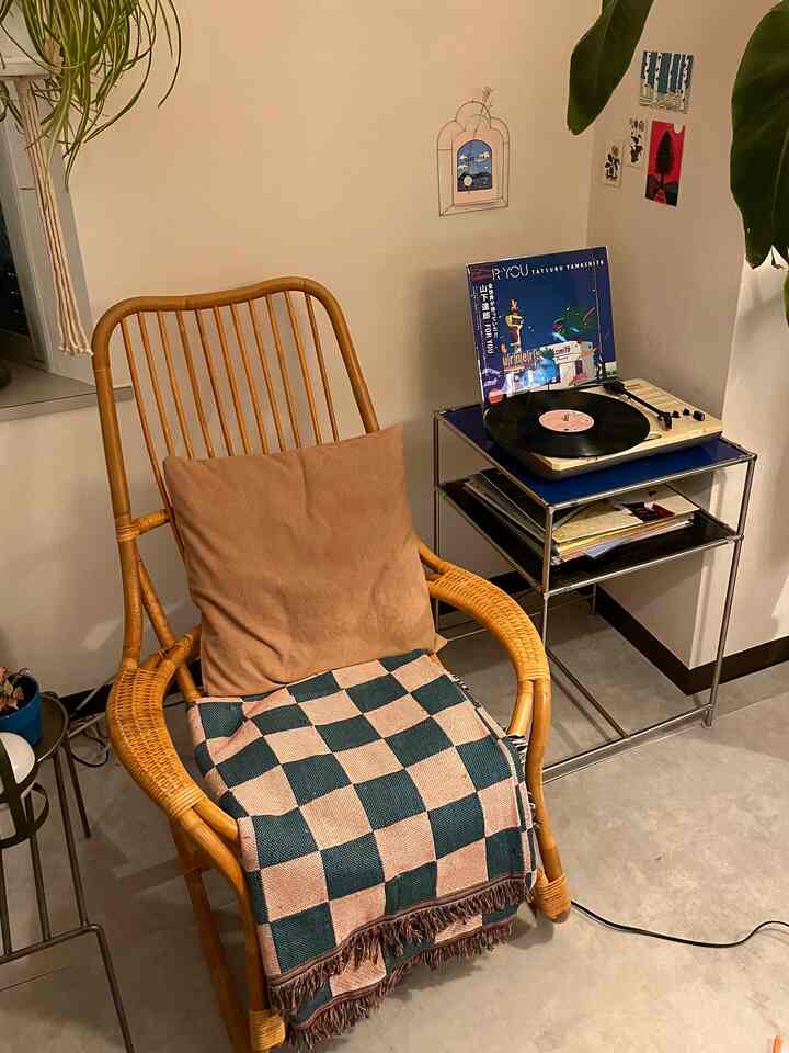 ナチュラルな色調のリビング、ラタン製ラウンジチェアとチェック柄のスロー、レコードプレーヤーが配置された雰囲気のあるインテリア