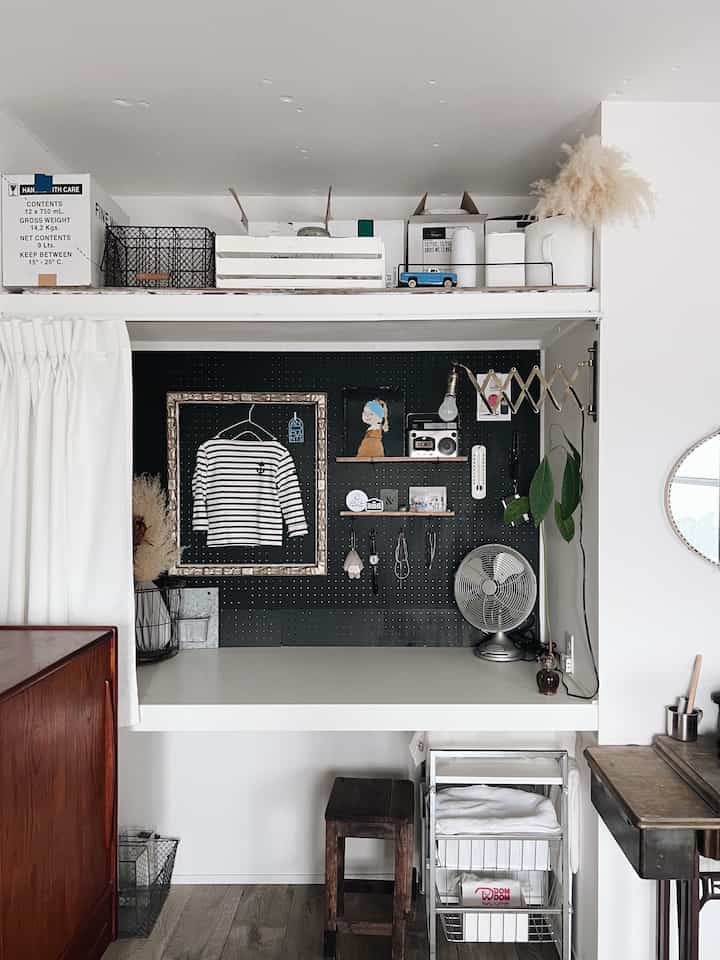 黒いペグボードと白いデスクが配置されたワークスペース、ヴィンテージの小物と整った収納が印象的な空間