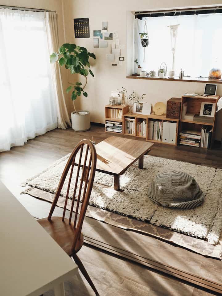 Warm natural-toned living room featuring a low wooden table, cushion, and bookshelf creating a cozy atmosphere