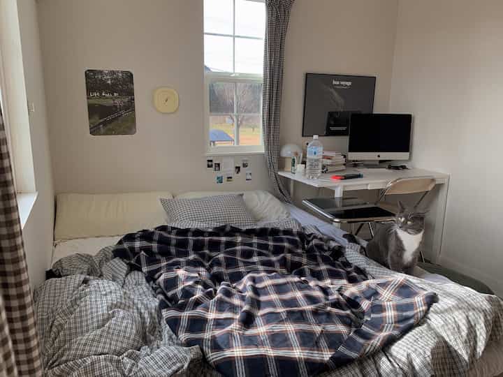 白を基調とした寝室にネイビーのストライプ布団、窓とデスクがあり自然とつながる雰囲気のある空間