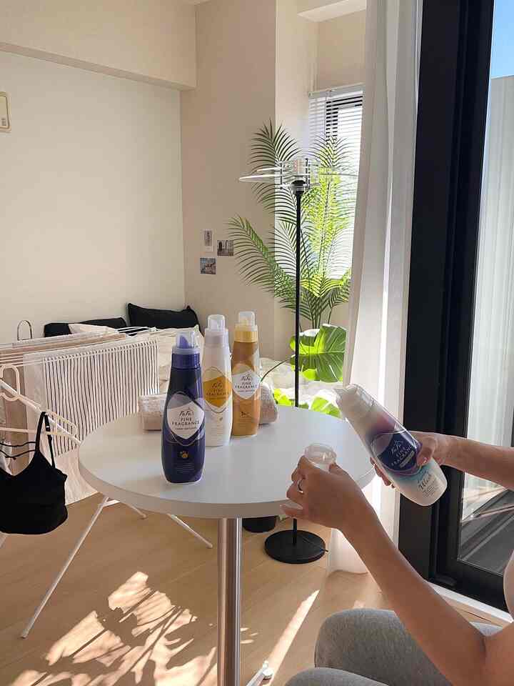 白と茶色のトーンのワンルーム、丸テーブルと植物、物干しスタンドが配置された印象的な空間