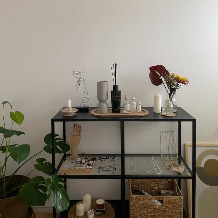 白い壁と黒のメタル棚が調和するナチュラルなリビング、植物とオブジェが配置されたミニマルなインテリア