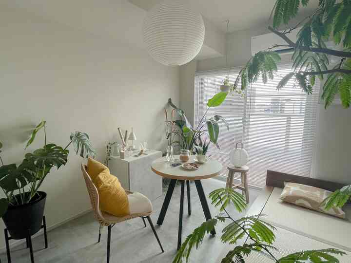 白と緑のトーンが調和した小さな円形の部屋、ラタンチェアと丸いテーブル、植物が自然な雰囲気を醸し出すインテリア