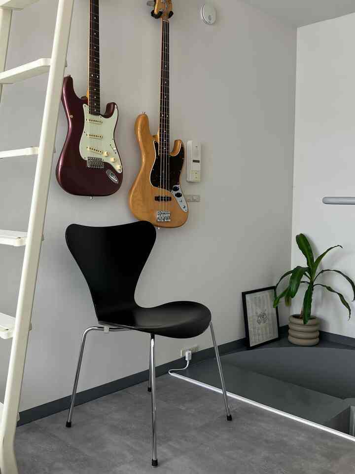 Minimal Nordic-style single household space featuring a black Series 7 chair and two guitars hanging on a white wall