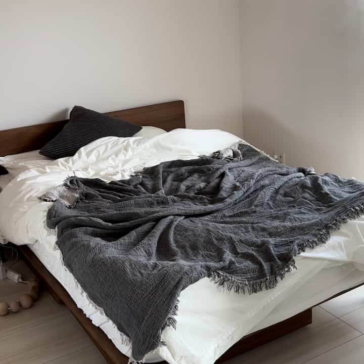 Natural tone bedroom featuring wooden bed frame with white bedding and gray blanket creating a cozy atmosphere