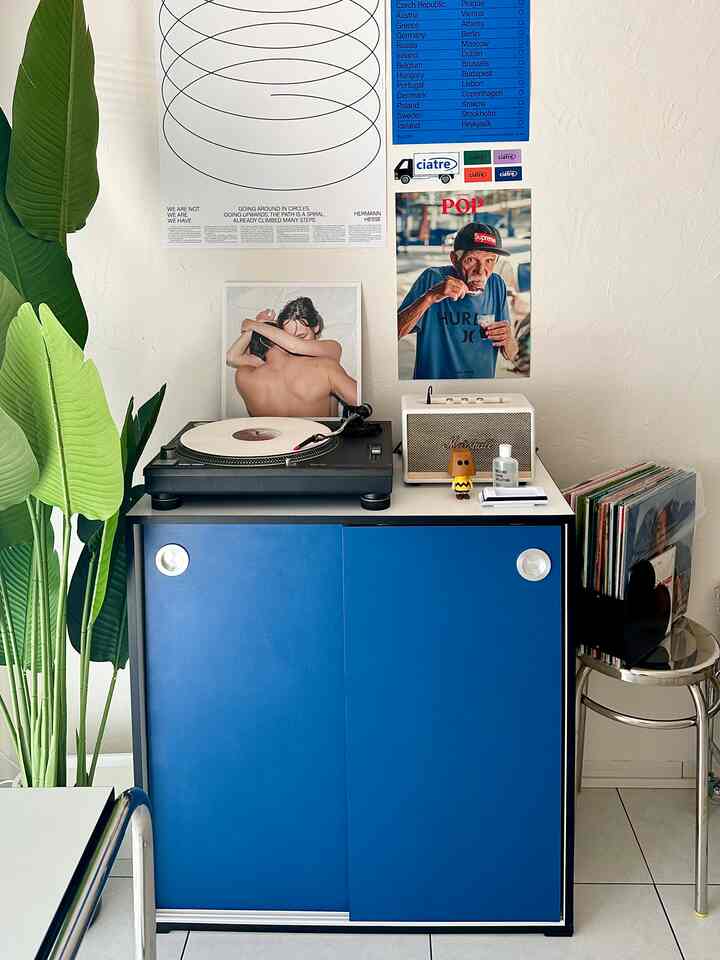 青い収納キャビネットが置かれたリビング、ターンテーブルとポスターが配された雰囲気のあるインテリア