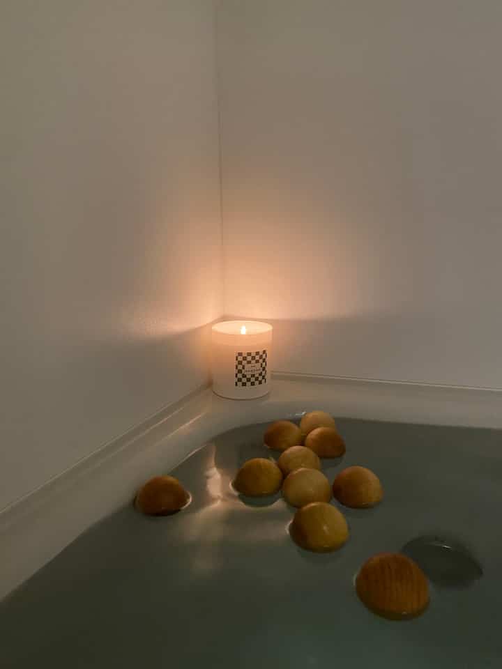 Softly lit bathroom corner with natural tones, wooden nuts floating on water and a lit candle creating a cozy atmosphere