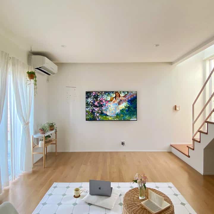 ナチュラルな色調のリビング、白い壁と木の床、TVが壁に掛けられ、コーヒーカップが置かれた雰囲気のあるおうちカフェ空間