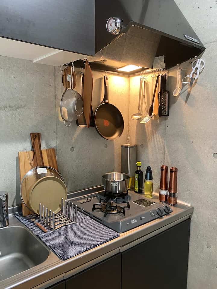 グレーのコンクリート壁とブラックのスチール調キッチン、調理器具が整然と配置されたコンテンポラリーなキッチン空間