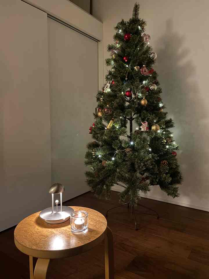 ナチュラルな色調の小さな空間、クリスマスツリーと照明が配置された雰囲気のあるインテリア