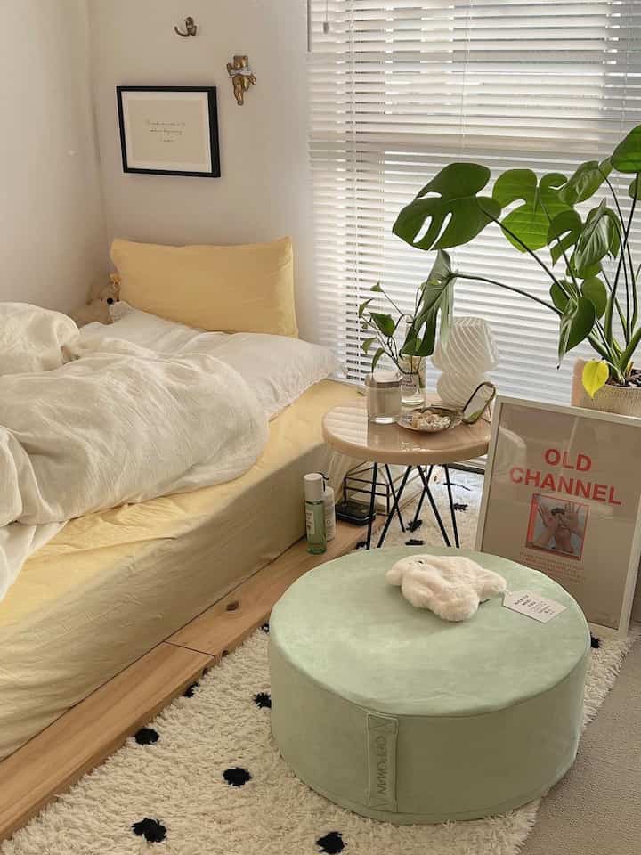 Bright, natural bedroom featuring a yellow bed and a light green ottoman with leafy plants