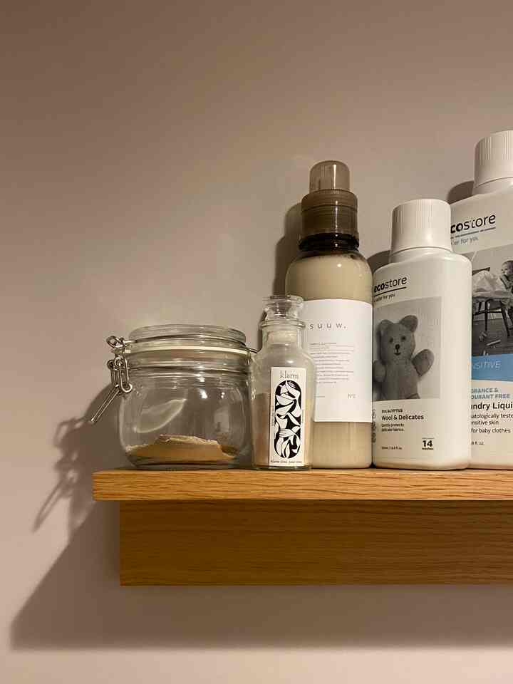 ナチュラルカラーと木目調の壁に取り付けられた棚にガラス容器と洗剤ボトルが置かれたバスルームの雰囲気のあるインテリア