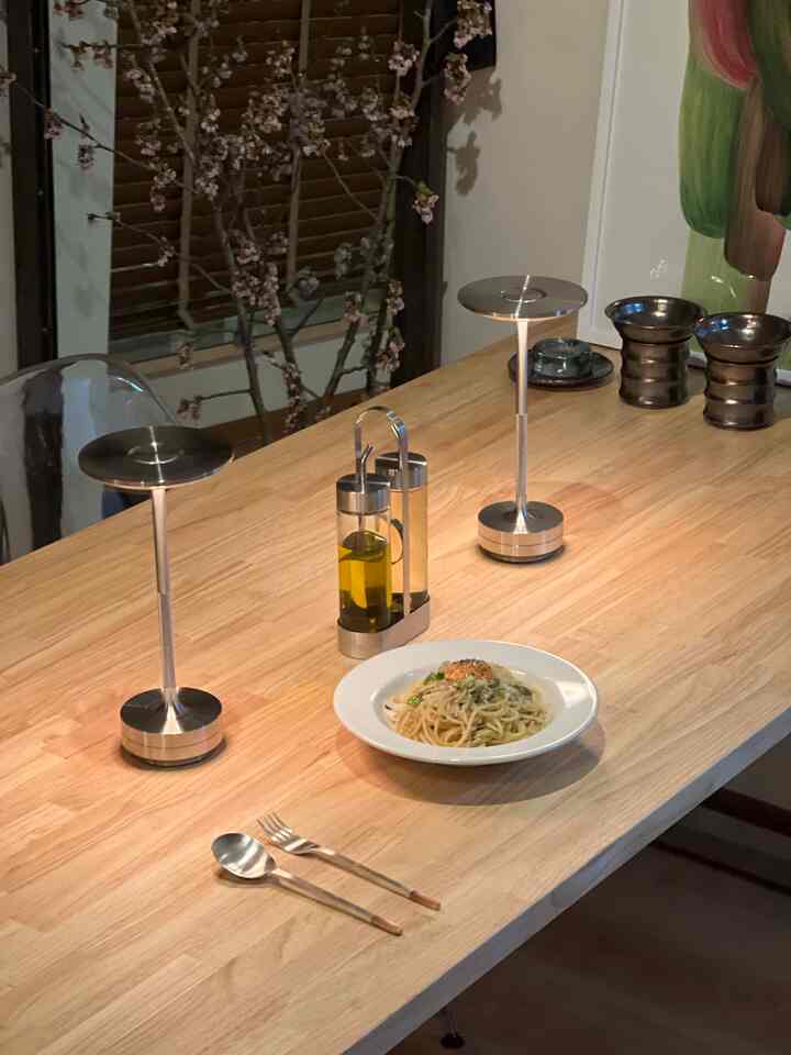 ナチュラルな木目調のダイニングルーム、シンプルなテーブルランプと皿、カトラリーが配置された雰囲気のある空間