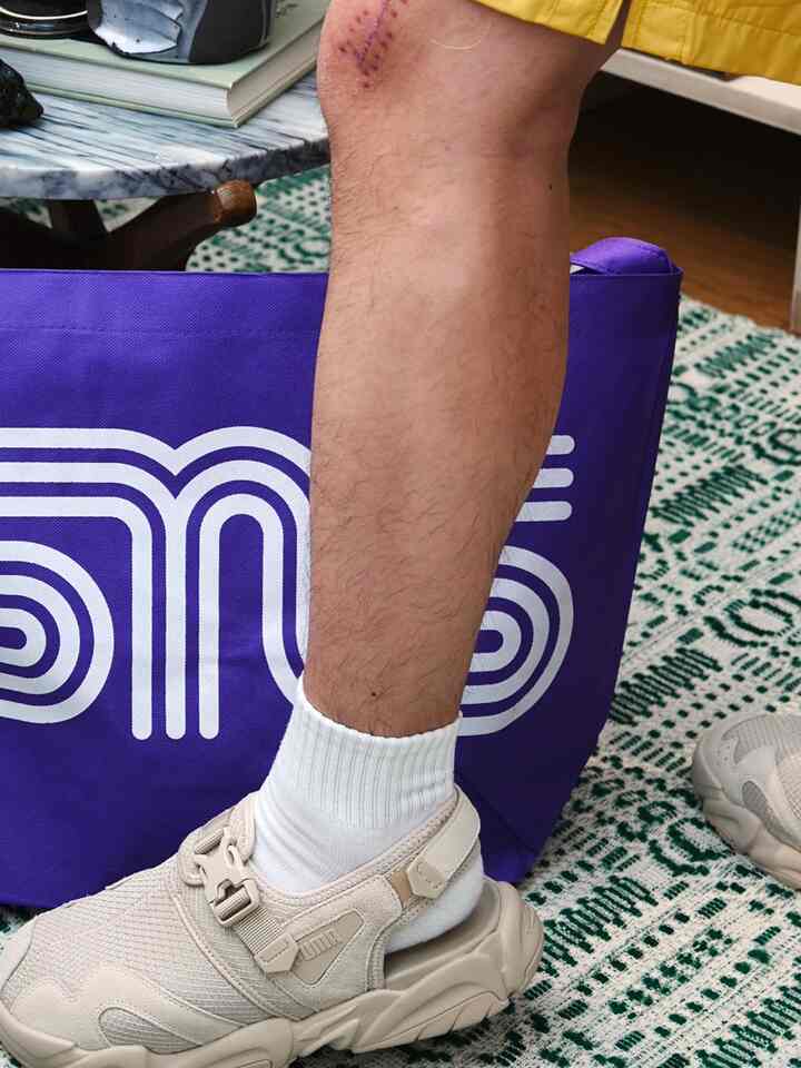 紫色のバッグと緑のパターンラグがある空間で、ベージュのスニーカーと白い靴下を履いた足が見える、室内履きの快適さを強調したインテリア