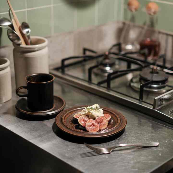 緑色のタイル壁とステンレスのカウンターがあるキッチン、お皿の上に無花果の料理と茶色のコーヒーカップが配置された雰囲気のあるおうちカフェ