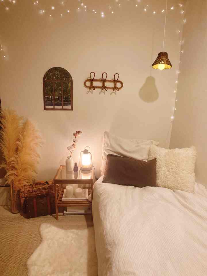 ベージュとホワイトの色調の寝室、ベッドとナイトテーブル、ストリングライトが配置された居心地の良い空間