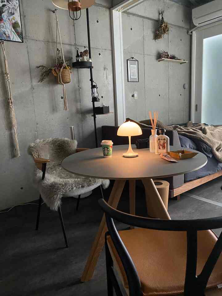 Natural modern living room with gray concrete wall and brown wood furniture, featuring warm table lamp and cozy armchair