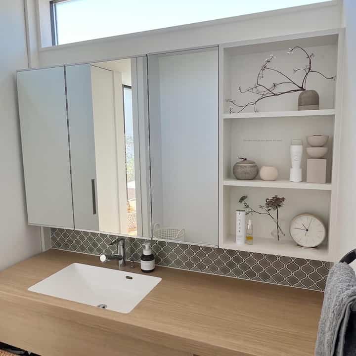 白とナチュラルな木目調が調和するバスルーム、大型ミラーとコーナー収納棚が清潔感のある印象的な空間