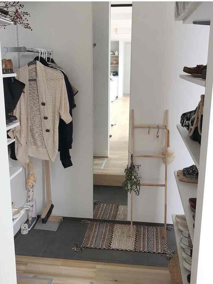 白い壁と木目調の床が調和した狭い玄関のシューズクローゼット、コートラックと靴棚が整然と配置されたナチュラルな空間