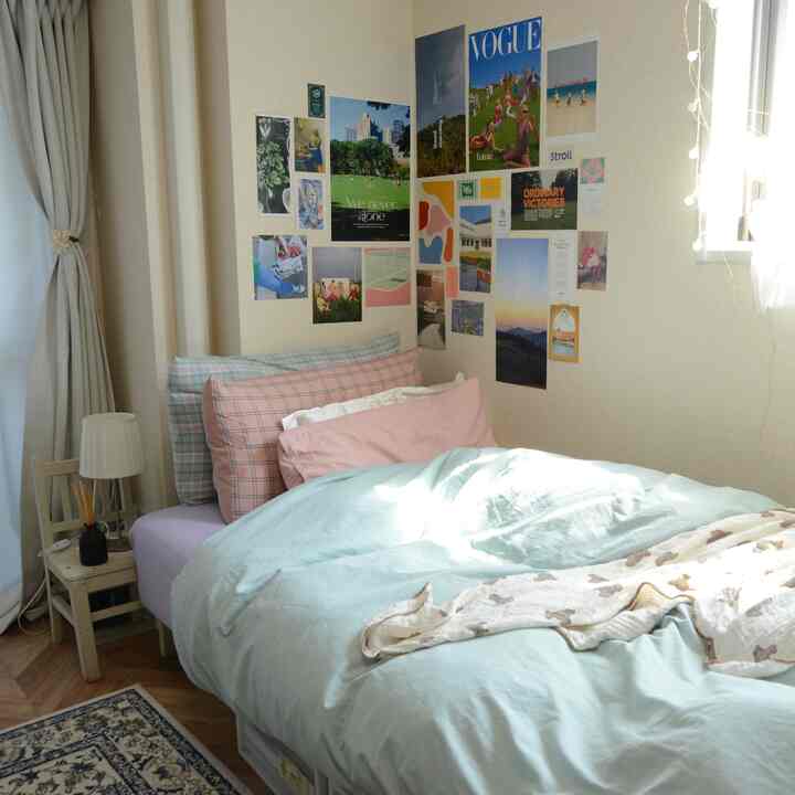 ベージュ色の壁とライトグレーのカーテンがある、ピンクとチェック柄の枕を配した快適な寝室のインテリア