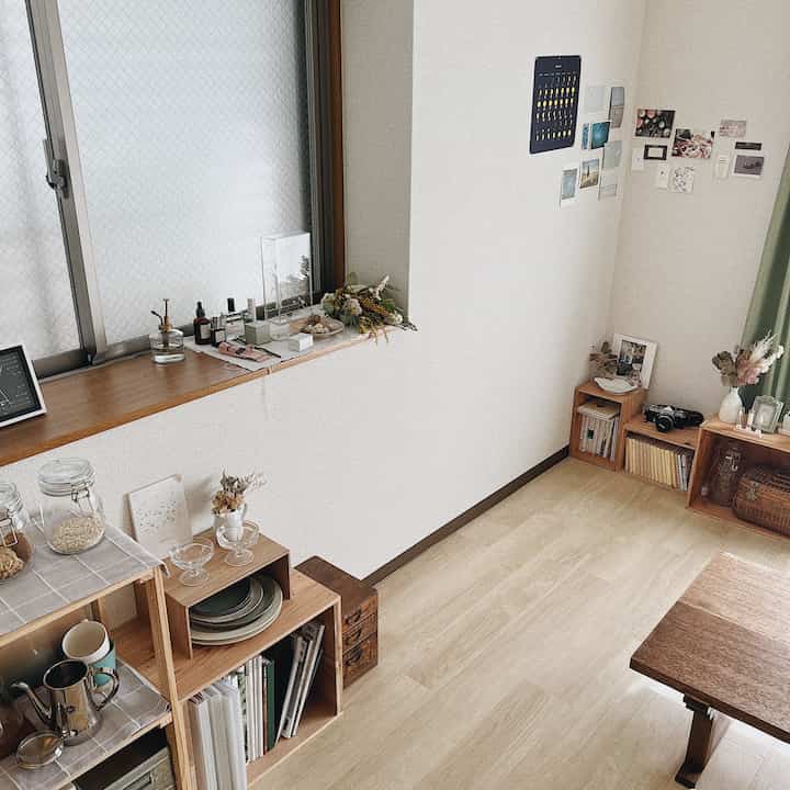 ナチュラルな木目調とベージュ色の小さなダイニングルーム、窓辺に透明な小物と整頓された収納棚が配置された温かみのある空間