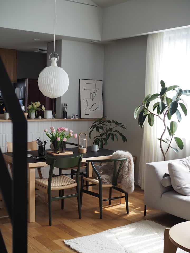 Natural wood tone dining room with green chairs and plants, featuring a pendant light and cozy atmosphere