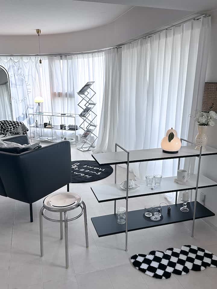 ホワイトとブラック、シルバーの色調のリビング、白いカーテンとモダンな棚、アームチェアが配置された印象的な空間