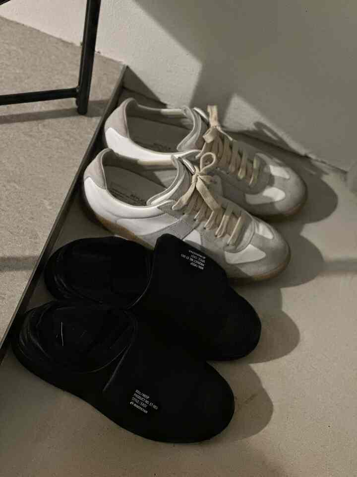 ベージュ色の床に黒いスリッパと白いスニーカーが並べられた玄関の空間