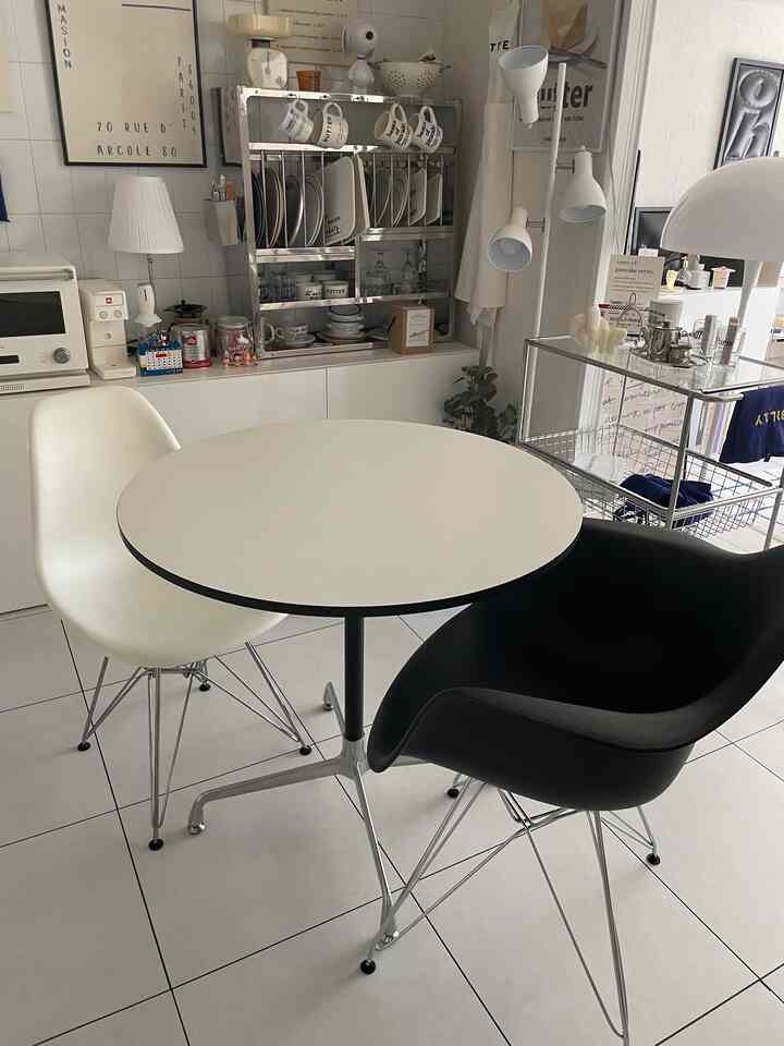 White-dominant compact kitchen space featuring a round table, black and white dining chairs, and organized shelving creating a neat atmosphere