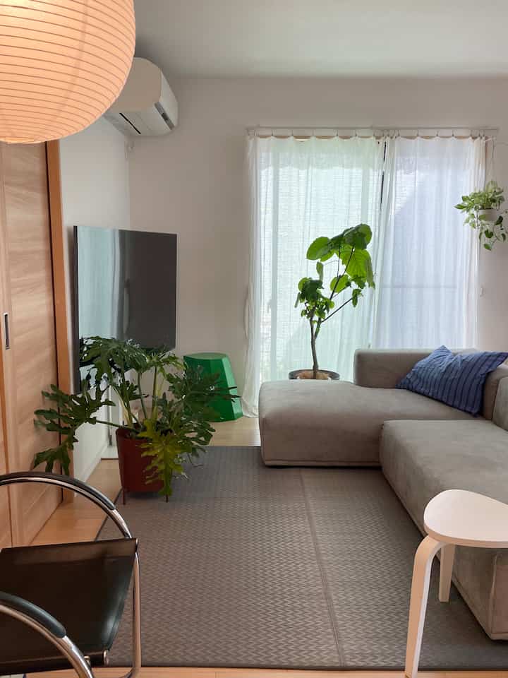 A white and natural toned living room featuring a beige sofa and green plants, creating a cozy atmosphere