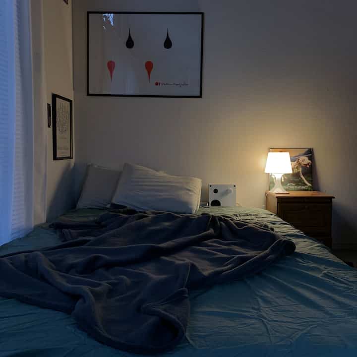 白と青のトーンの寝室、青い掛け布団カバーと濃いブランケットをかけたベッド、ナイトスタンドのテーブルランプが置かれた雰囲気のあるインテリア