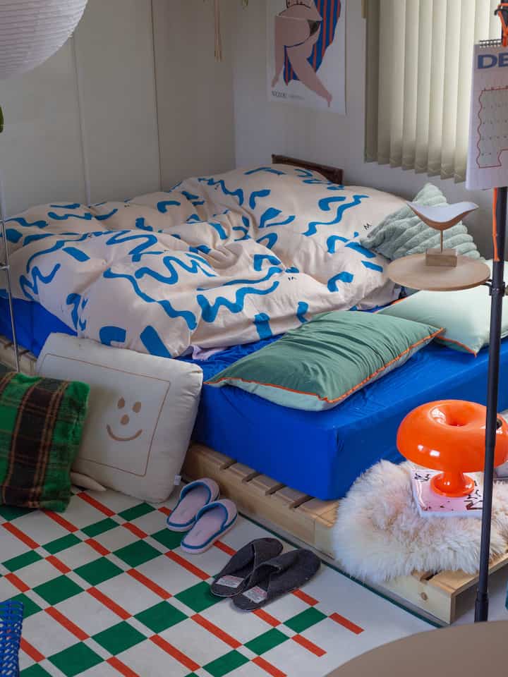 Cozy bedroom space featuring blue and green bedding with a green and red checkered rug