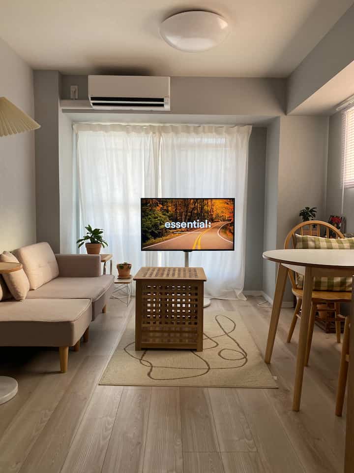 ナチュラルなベージュと木目調が特徴のリビング、テレビ台やソファ、丸いダイニングテーブルが調和した雰囲気のあるインテリア