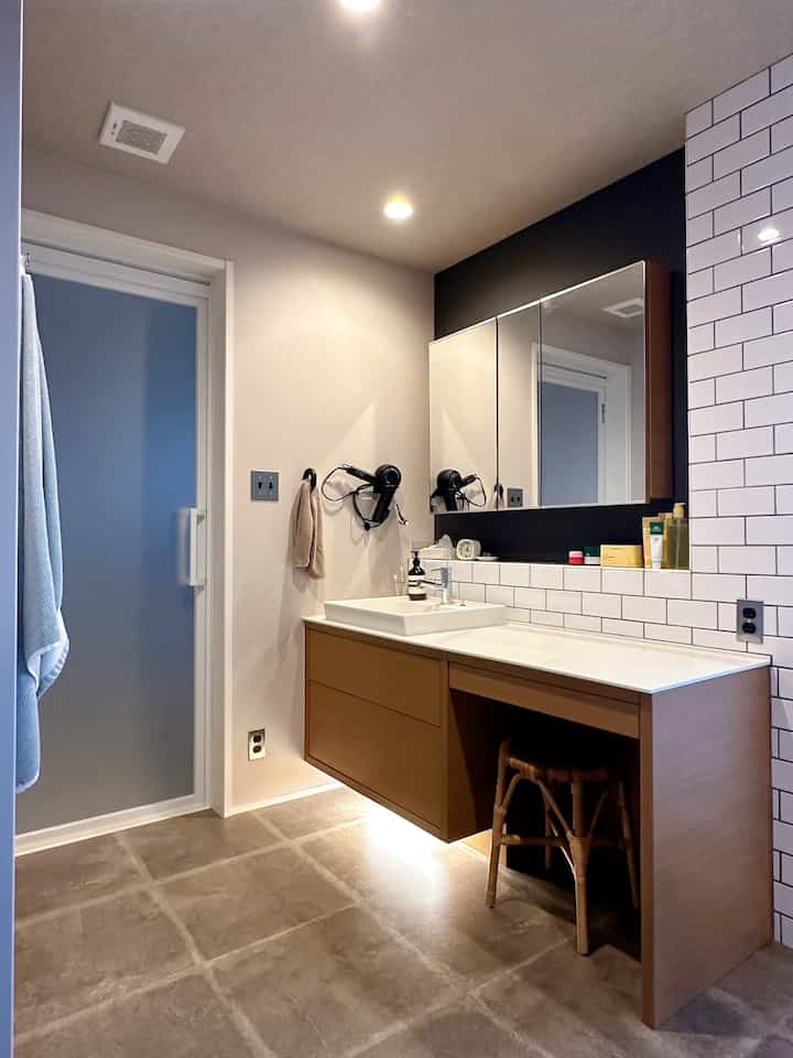 白と茶色のトーンのバスルーム、ミニマルなスツールと大きな鏡が配置され、ホテルライクな雰囲気のあるインテリア