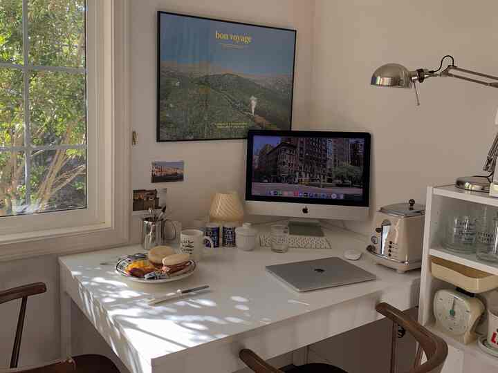 白とナチュラルカラーのキッチンスペース、白いデスクにパソコンと朝食が置かれた雰囲気のあるインテリア