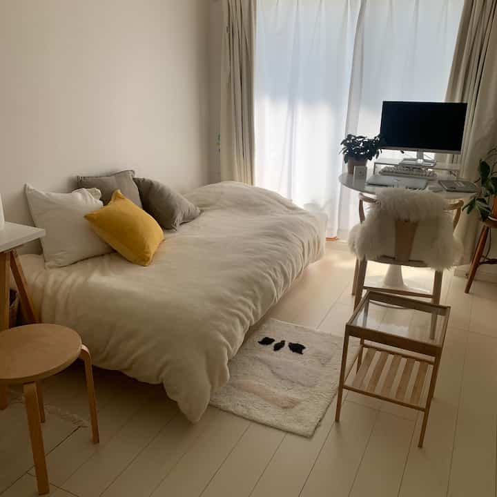 Bright white and beige 1K bedroom featuring a bed with cushions and a compact home office desk creating a cozy atmosphere