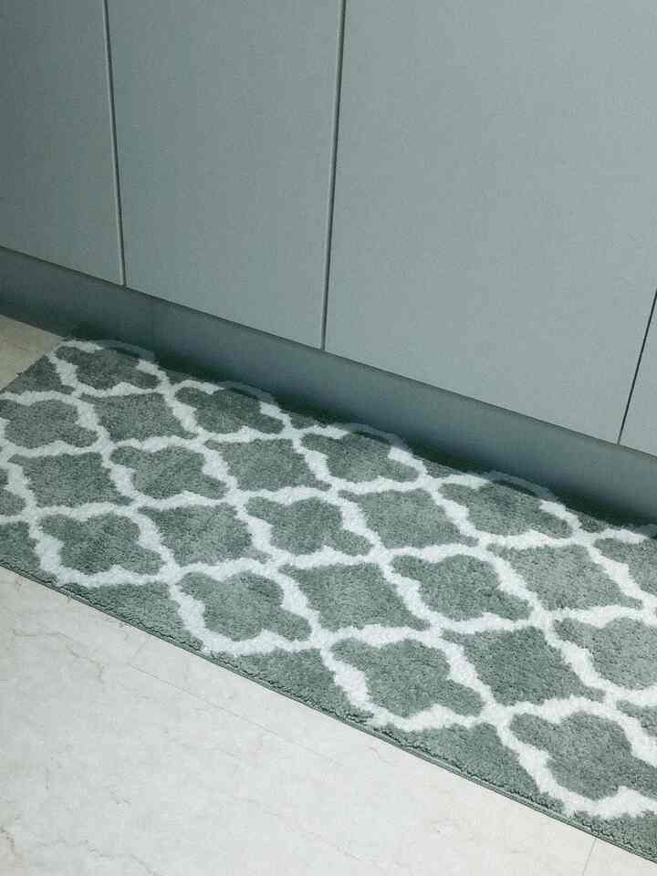 A kitchen space in green and gray tones featuring a patterned non-slip rug on the floor.