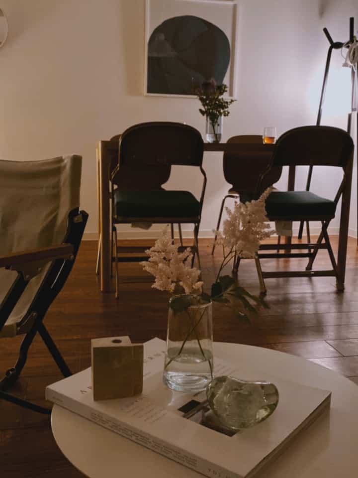 Warm natural-toned living room featuring wood-toned dining table and chairs, with a coffee table and vase arranged for cozy atmosphere