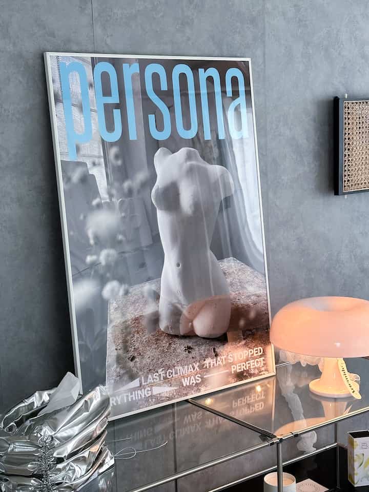 グレーの壁を背景に、白い胸像のポスターとピンクのテーブルランプが置かれたモダンなリビングコーナー