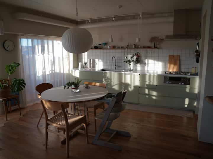 Natural tones and white tiled kitchen with dining table and a child’s high chair, creating a cozy home environment