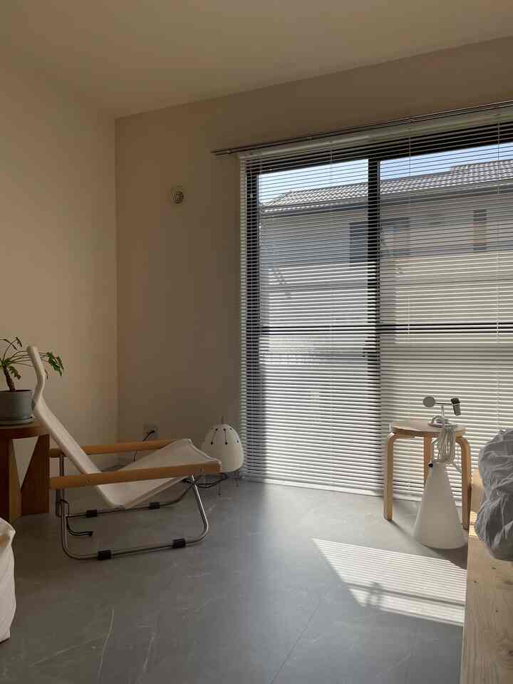 暖かいベージュとホワイトの色調のリビング、木製フレームのアームチェアとウッドスツールが配置されたナチュラルなインテリア