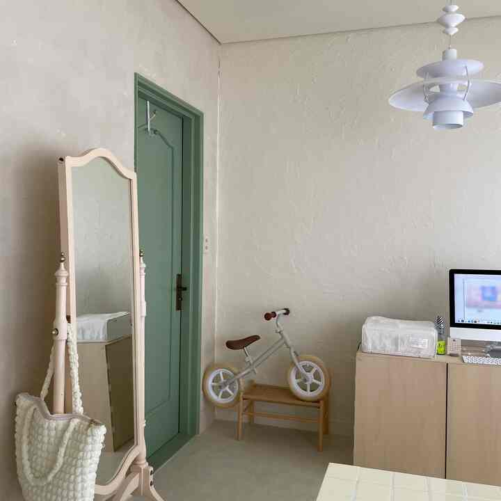 ナチュラルな色調の子供部屋、緑のドアとラタンベンチの上に子供用自転車が置かれた雰囲気のある空間