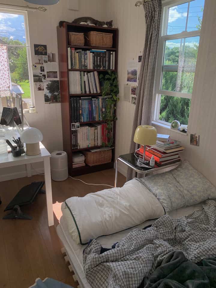 Bright white and beige small single household bedroom featuring a bookshelf, bed, and desk for a cozy home office atmosphere