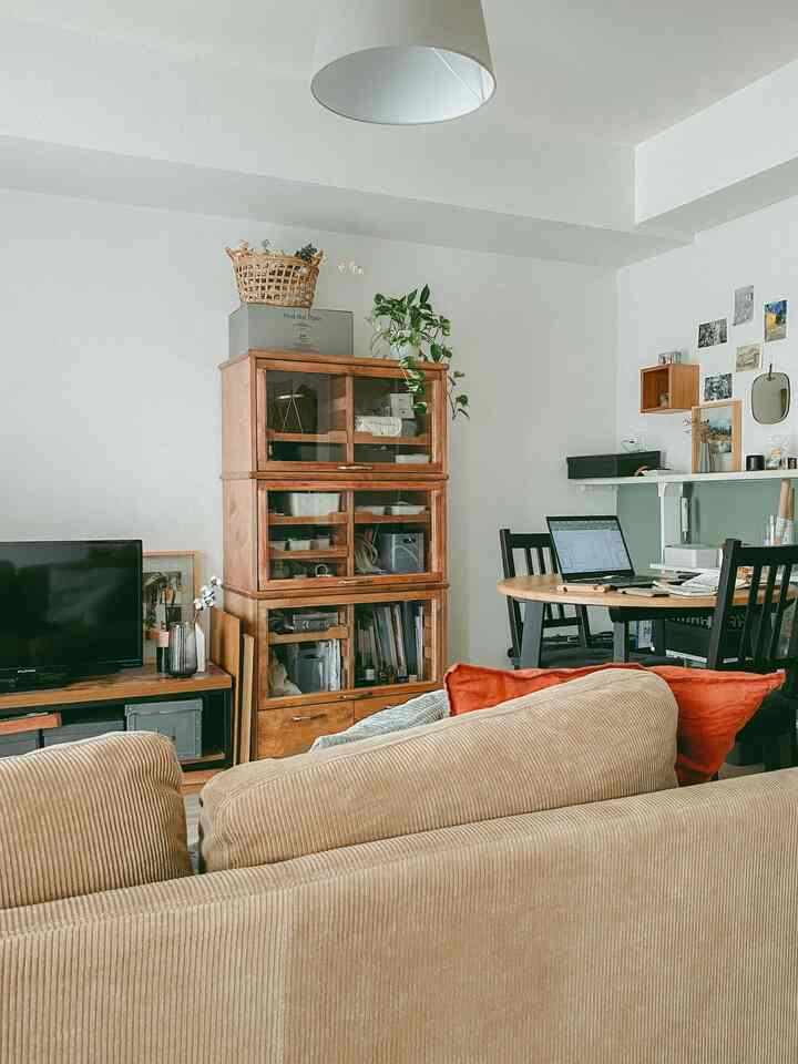 白い壁と茶色の木製家具が並ぶ1LDKのリビング、ベージュのソファと丸いダイニングテーブルがある落ち着いた雰囲気の空間