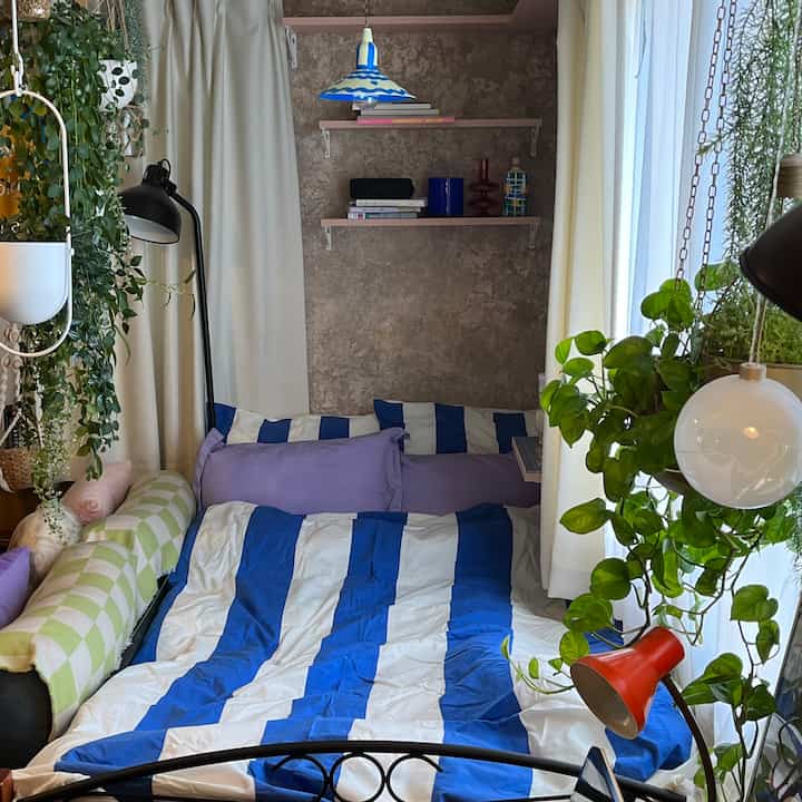 ブルーとホワイトのストライプ柄の寝具がある寝室、多数の植物とボヘミアンスタイルのインテリアが調和した雰囲気のある空間