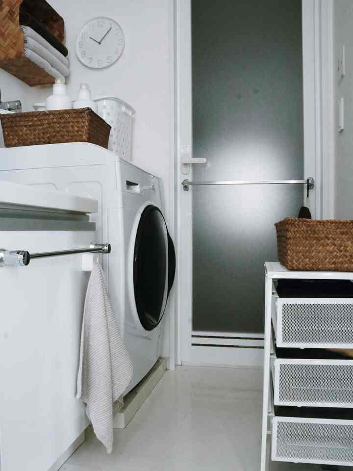 白を基調としたバスルーム兼ランドリー、ドラム式洗濯機と収納棚が配置されたシンプルで清潔感のあるインテリア