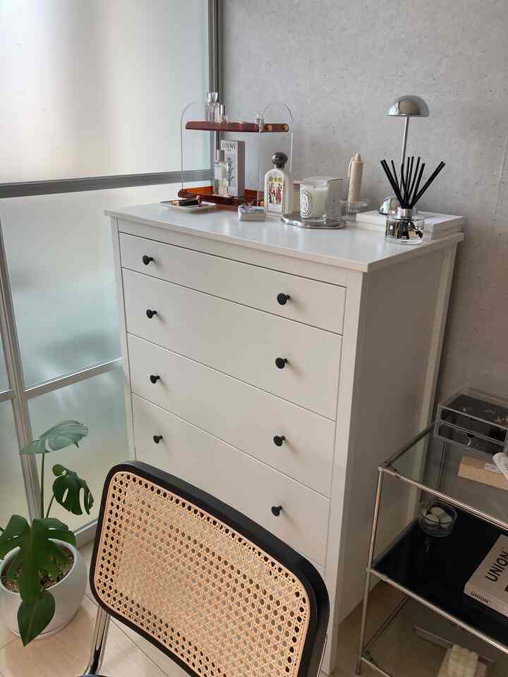 白とナチュラルカラーのリビング、白いチェストとラタンの椅子、植物が配置されたミニマルな雰囲気の空間