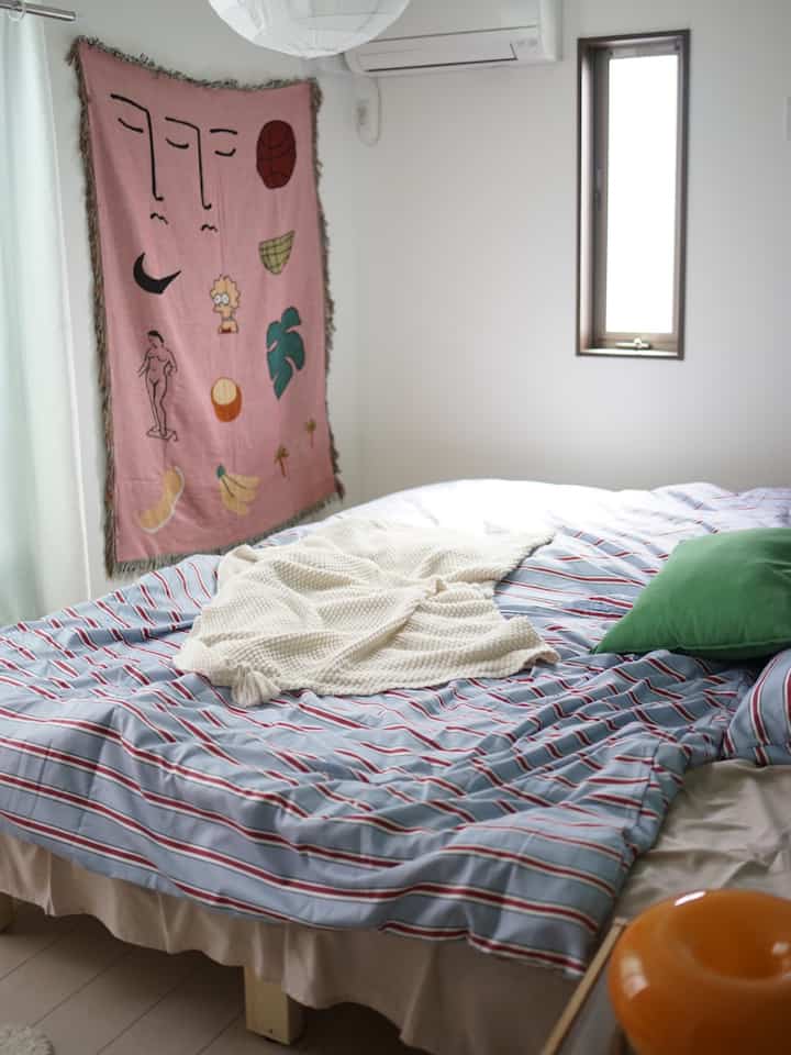 Pastel-toned bedroom featuring striped duvet cover, ivory blanket, and a pink abstract fabric art on the wall creating a simple atmosphere