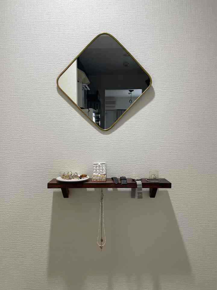 White wall with gold framed mirror and dark wood tone shelf in a neat entrance space