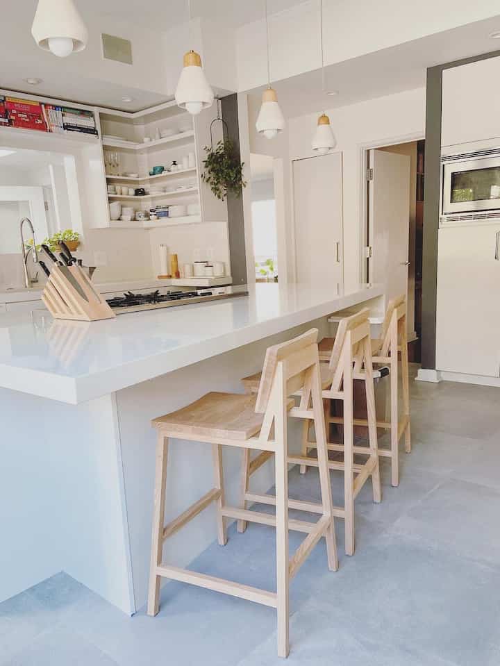 White and wood tone kitchen featuring oak bar stools and pendant lights in a clean, modern setting